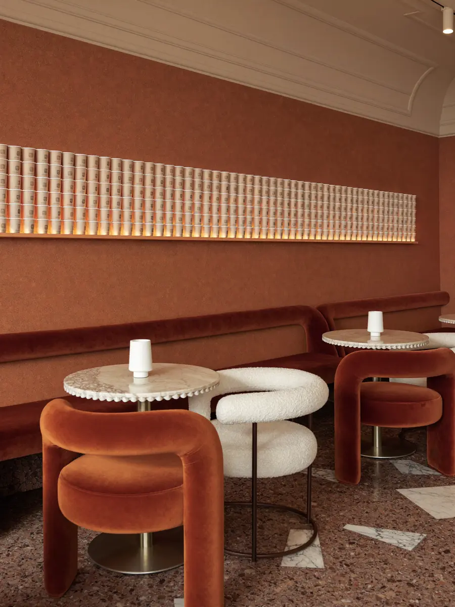 Banqueta de terciopelo teja con mesas redondas de mármol y una fila de vasos iluminados en la pared