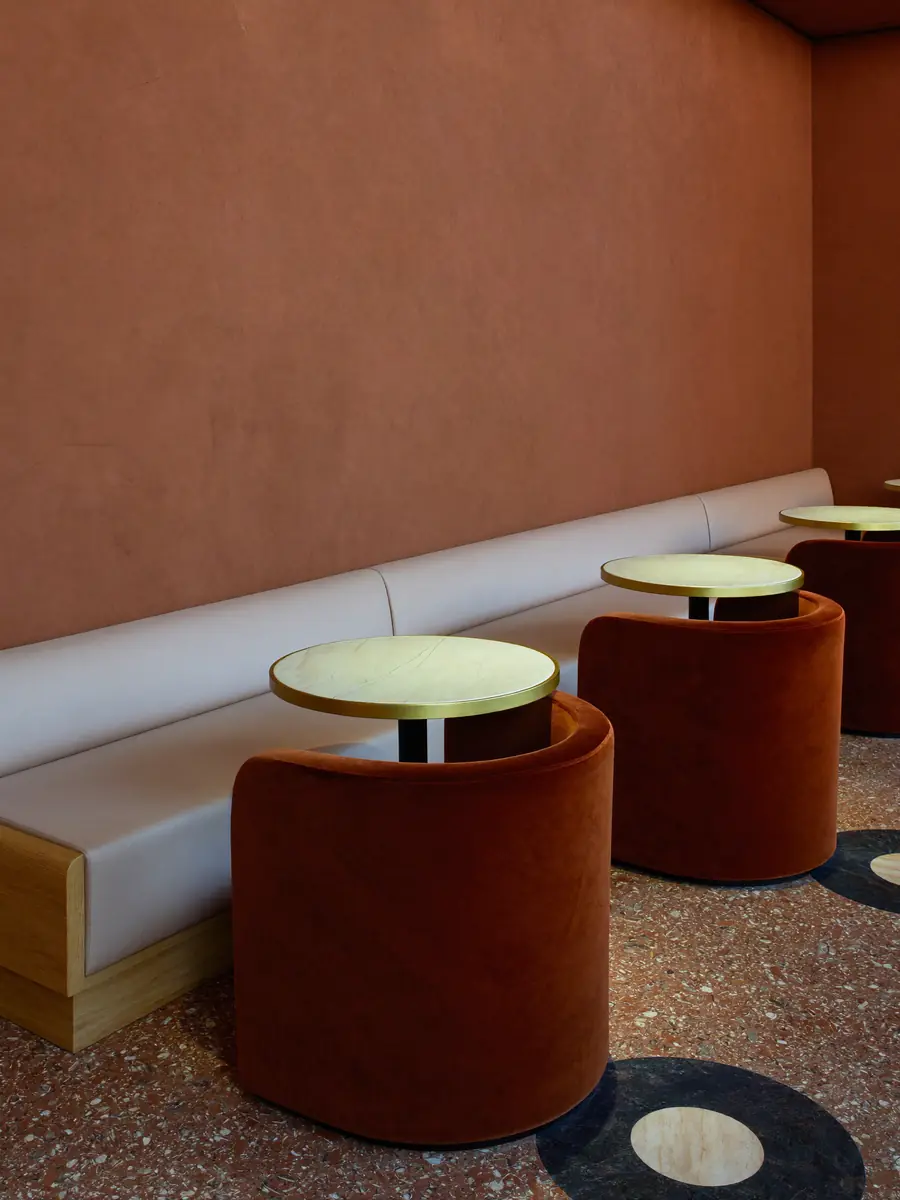 Sillones de terciopelo teja junto a mesas redondas verdes con borde dorado
