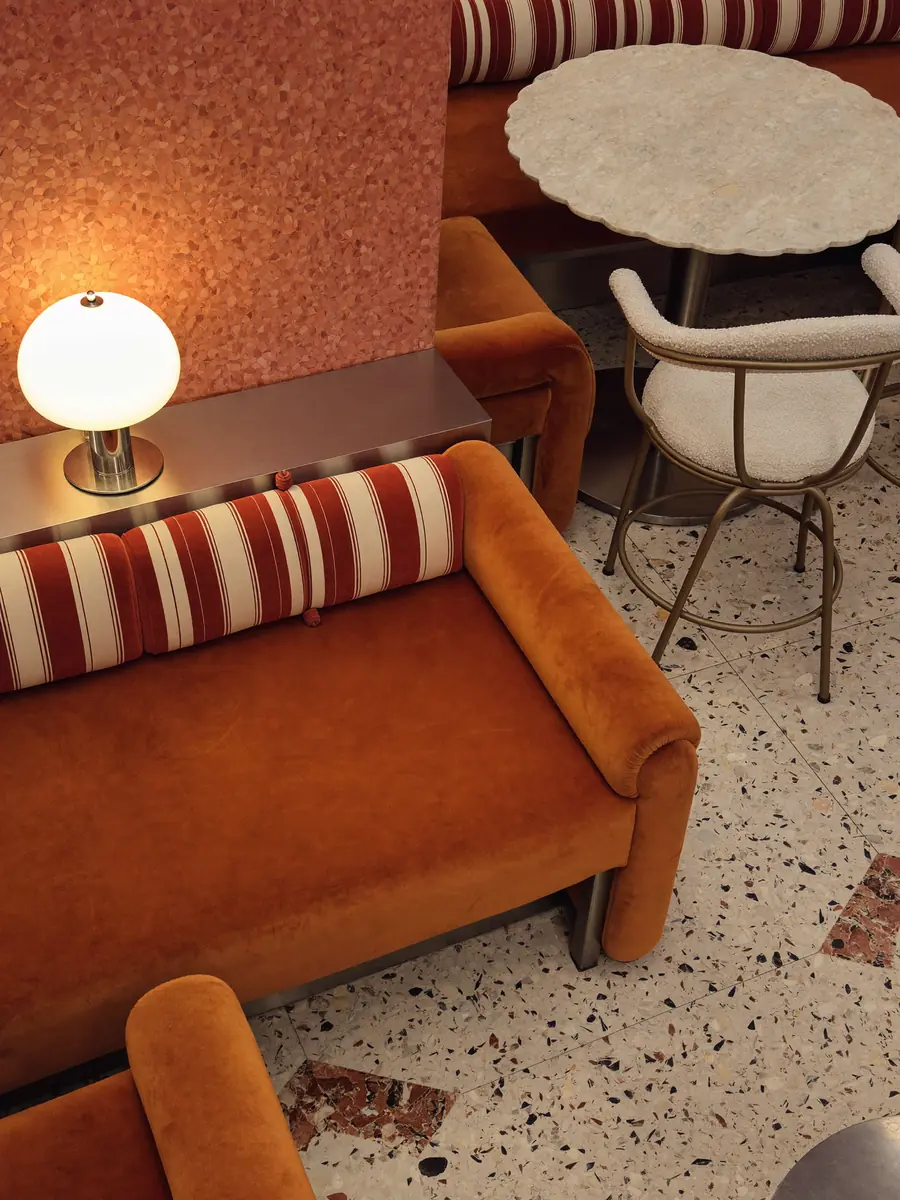 Sofá de terciopelo naranja con almohadón a rayas junto a una lámpara de mesa encendida