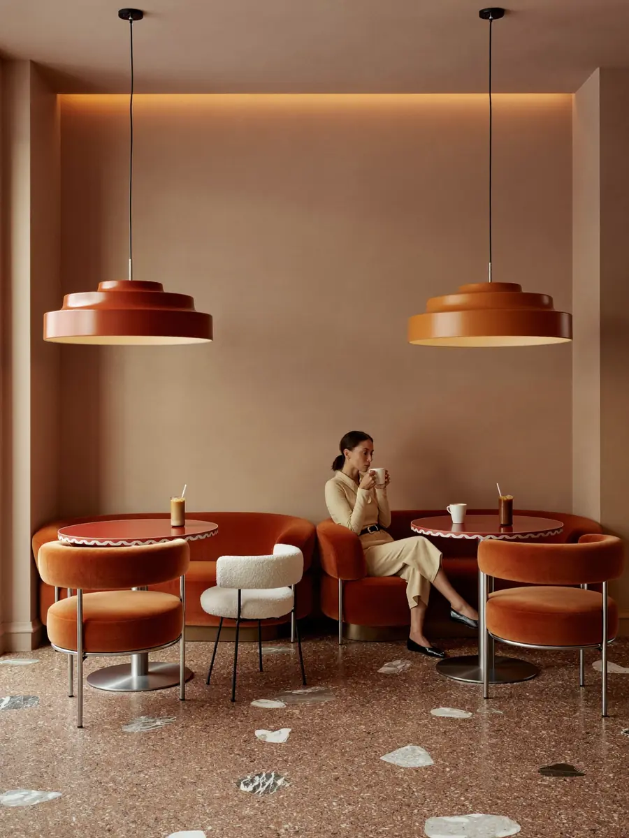 Mujer tomando un café en un rincón con sillones de terciopelo y dos lámparas colgantes color teja